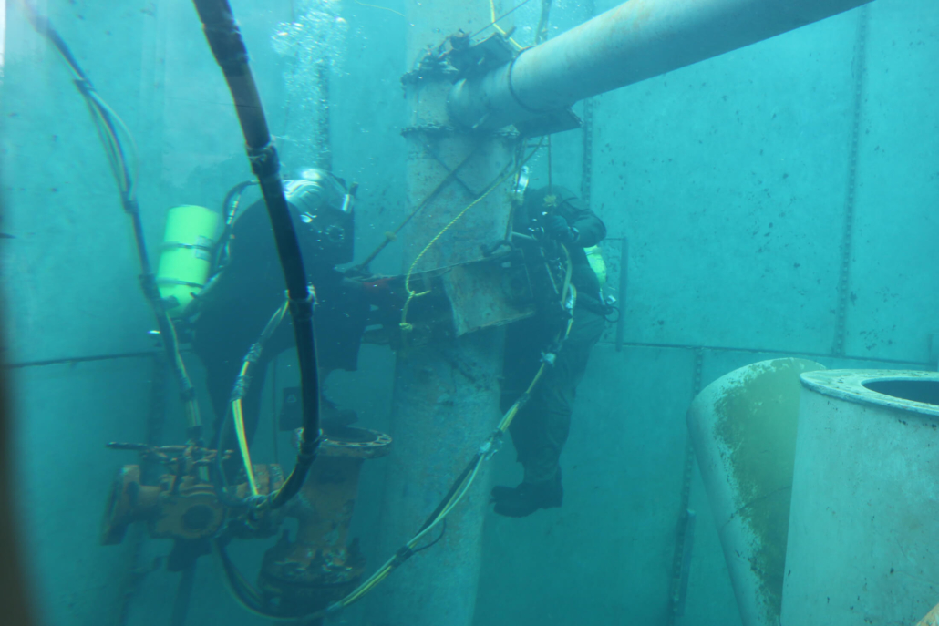 Two commercial divers in a training pool practicing working on pipeline repairs.