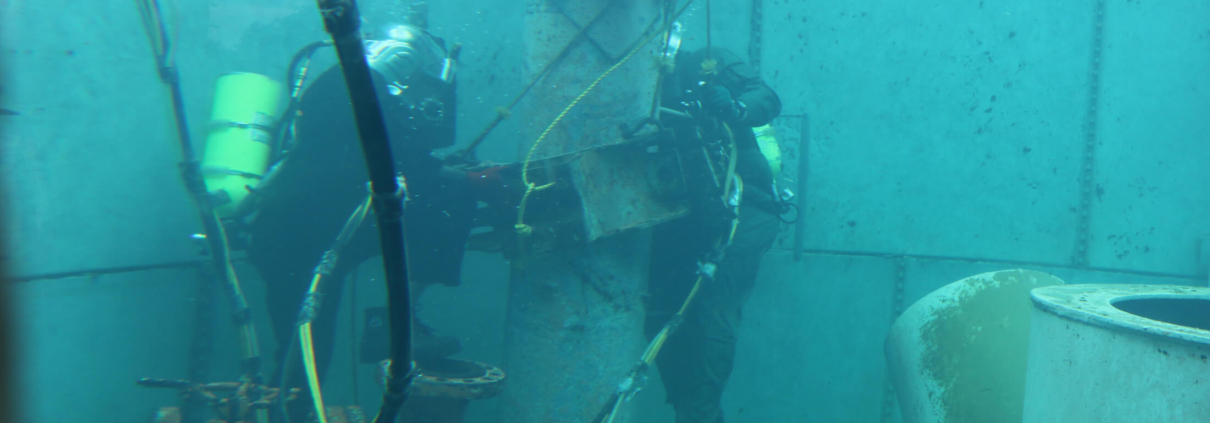Two commercial divers in a training pool practicing working on pipeline repairs.
