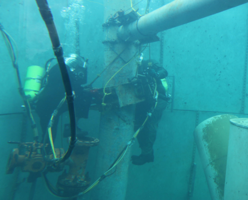 Two commercial divers in a training pool practicing working on pipeline repairs.