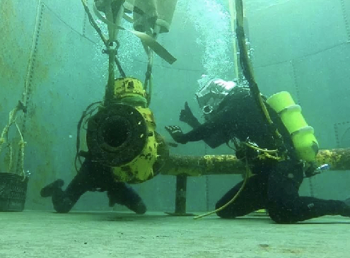 Two commercial divers in a training pool working on fixing a pipe.