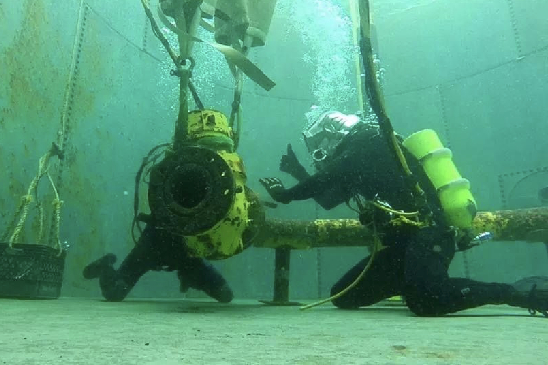 Two commercial divers in a training pool working on fixing a pipe.