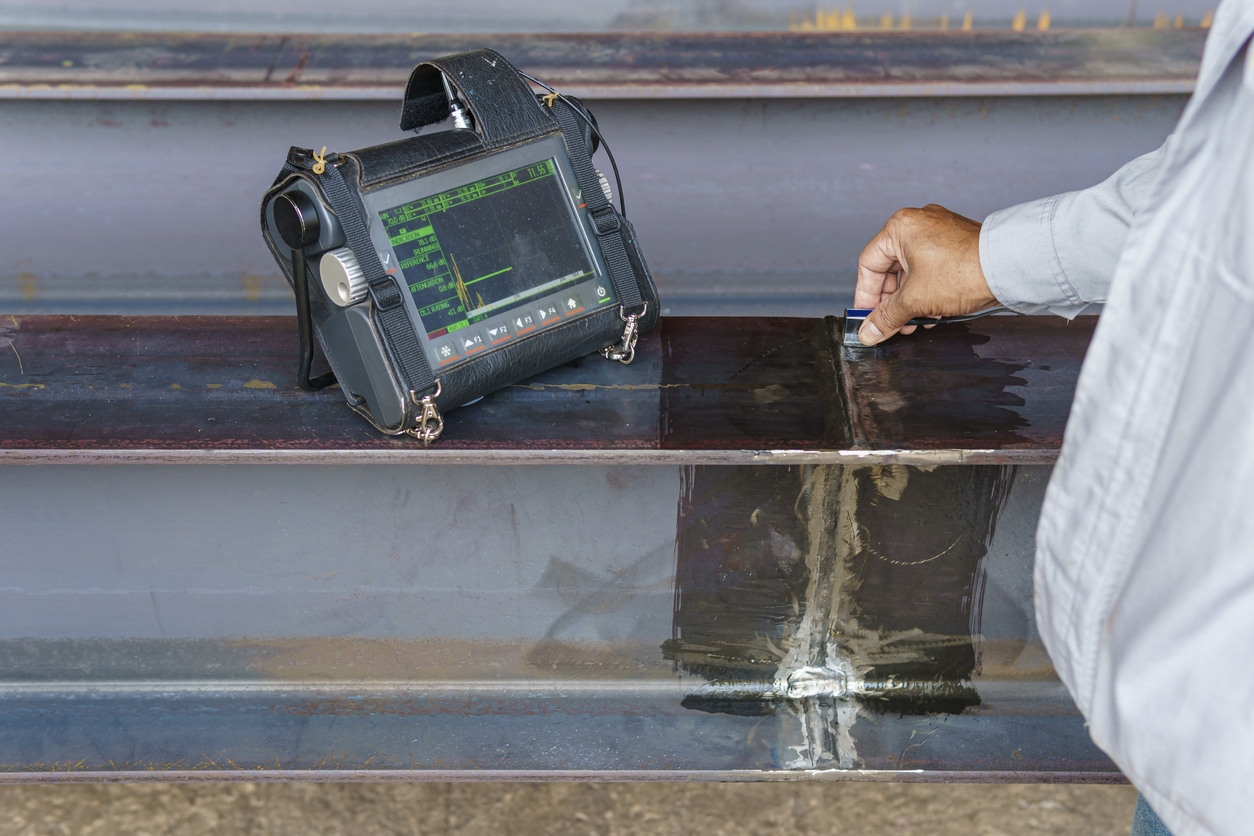 A man working on a steel frame uses NDT inspection tools to evaluate structural integrity