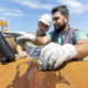 Technicians wearing safety gear performing a non destructive testing inspection on industrial equipment with a corrosion testing tool.